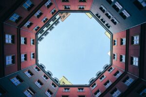 Upward view of symmetrical urban buildings showcasing a clear blue sky through a geometric frame.