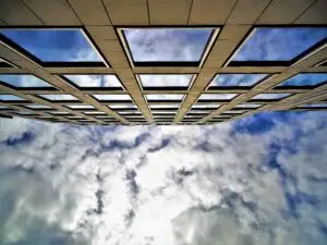 Low angle view of a building facade with glass windows reflecting a cloudy sky, emphasizing modern architecture.